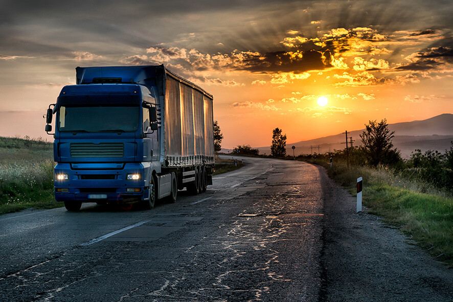 Blue lorry truck on the asphalt rural road in a beautiful sunset