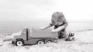 Un garçon joue avec son camion sur la plage - noir et blanc