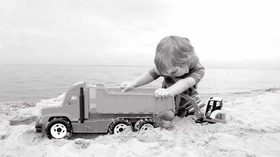 Un garçon joue avec son camion sur la plage - noir et blanc