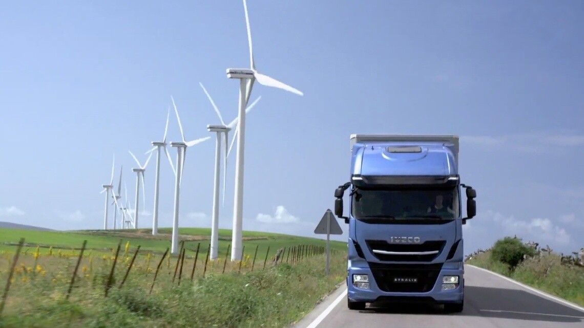 Un camion bleu sur une route traversant un champs d'éoliennes