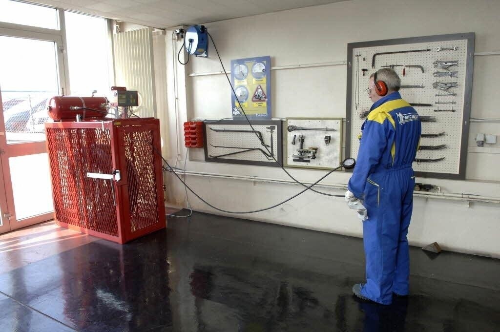 Technician inflating a commercial tire from a safe distance while the tire is secured in an inflation cage