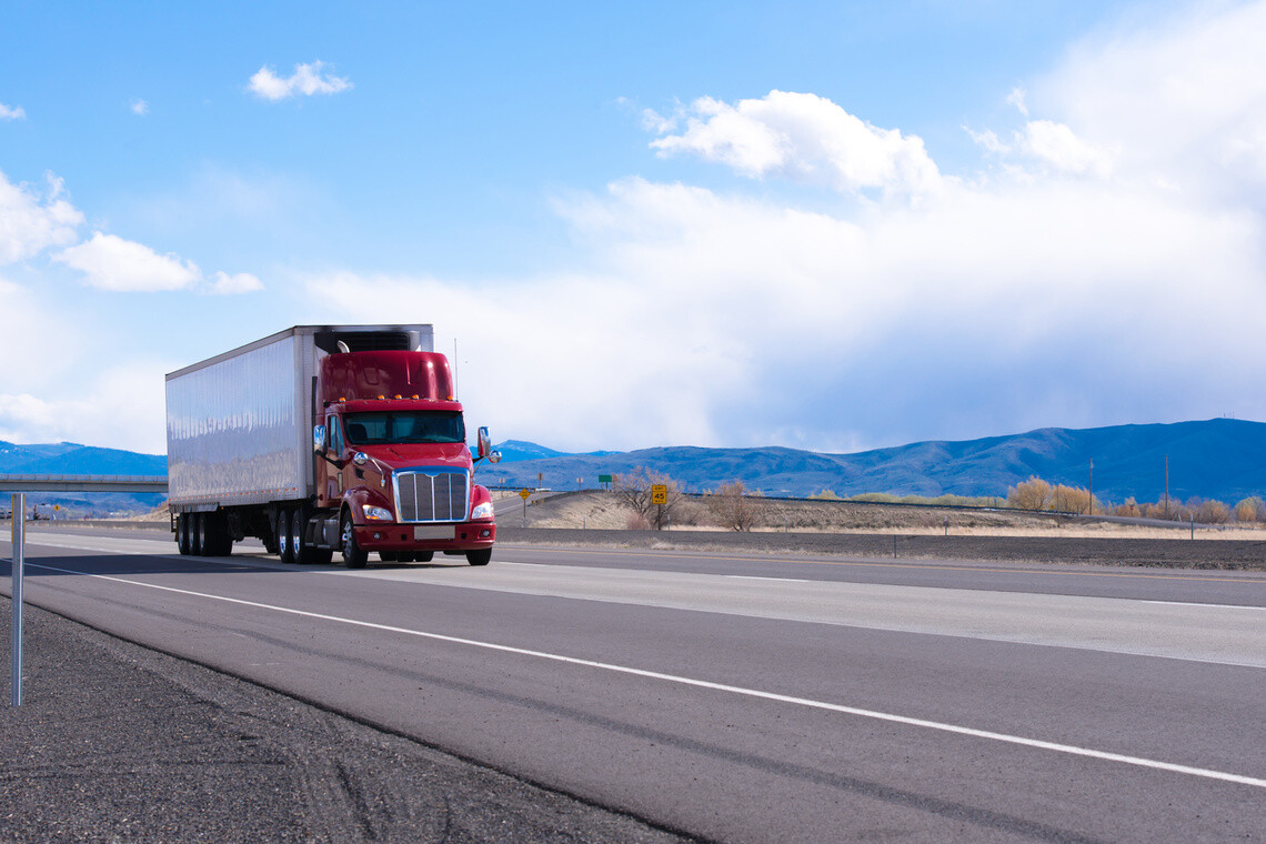 Big rig American bonnet powerful red semi truck with refrigerated semi trailer with refrigerator unit for cooling trailer inside space transporting commercial cargo on flat road in Utah