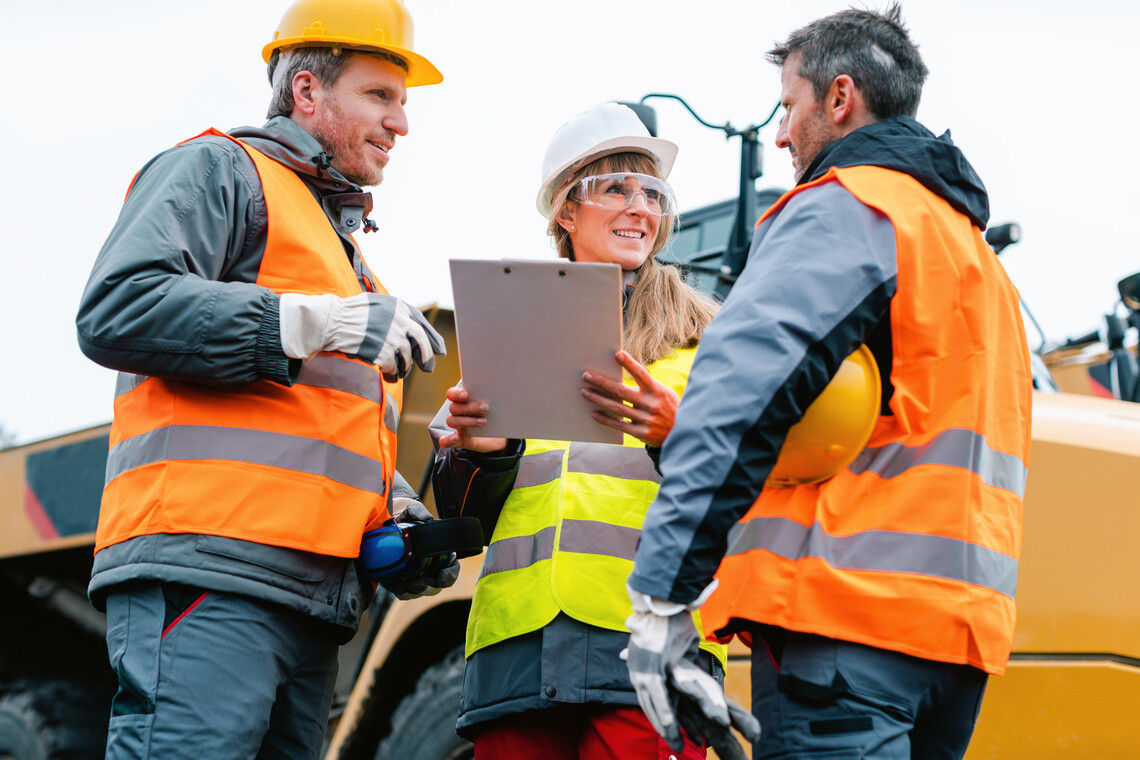 Three workers in a quarry discussing in front of heavy machinery looking at plan