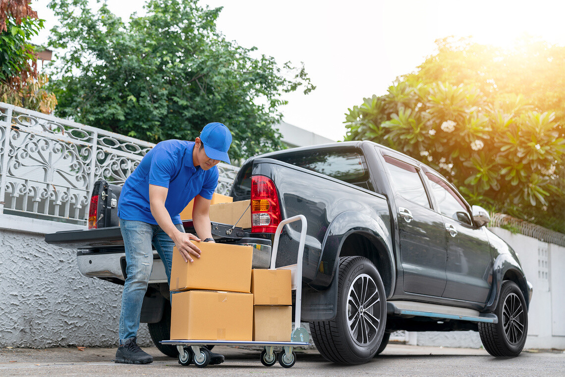 Delivery men in red uniform unloading cardboard boxes from pickup truck. Courier man sending the parcel or package to the customer on a business day. Online shopping and transport logistics concept."n
