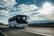 Long-distance bus traveling on road with blue sky and clouds