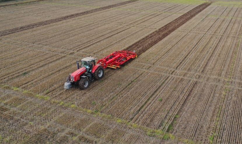 Tractor driving through field pulling implement behind it