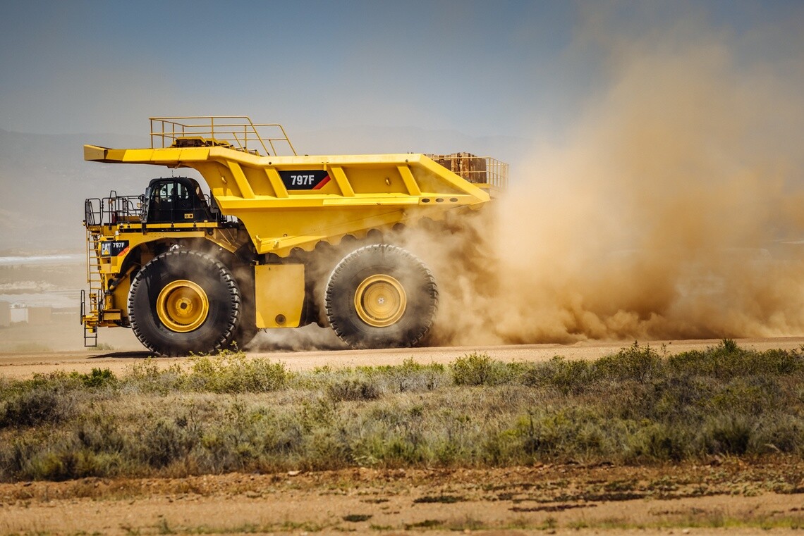Yellow mine equipment driving with cloud of dust behind it