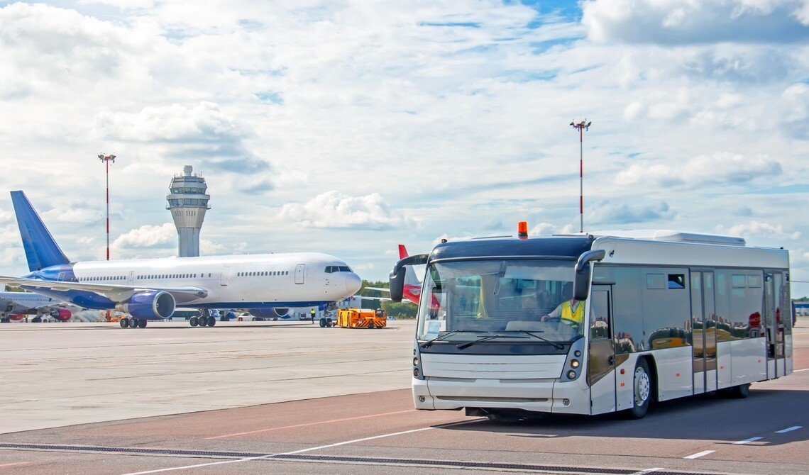 shuttle bus driving on tarmac with airplane and air traffic control tower in background