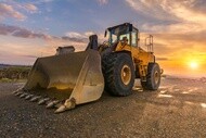 wheel loader working on dirt with sunset in background