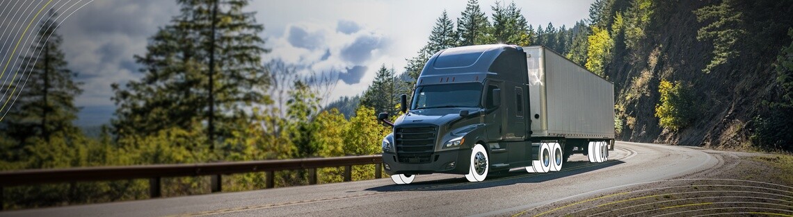 Blue cabbed semi truck driving down highway with forest in background. Truck has white overlay on its tires