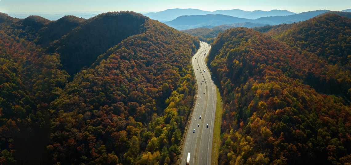 Aerial view of vehicles on a highway with trees on either side and mountains in the distance