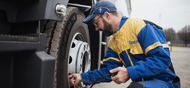 Man in yellow and blue Michelin mechanic jumpsuit putting air in the tire of a semi truck