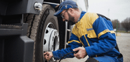 Man in yellow and blue Michelin mechanic jumpsuit putting air in the tire of a semi truck