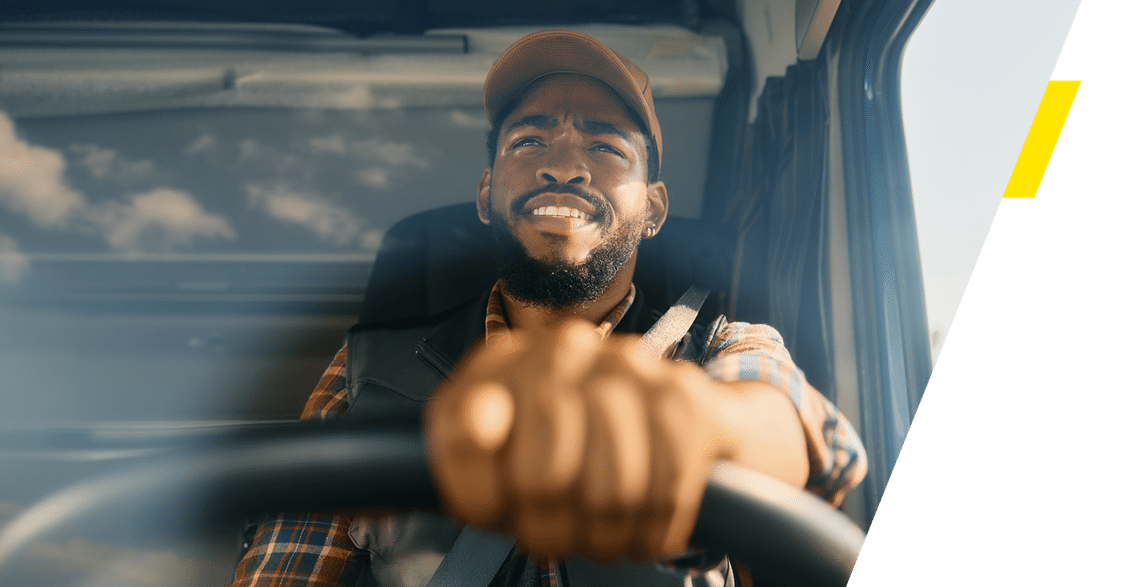 Looking into the cab of a truck where an African American truck drive is holding onto the steering wheel as he drives.