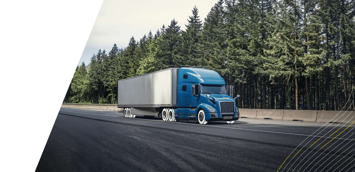 Blue semi truck with white trailer and white overlay on tires driving on wooded highway