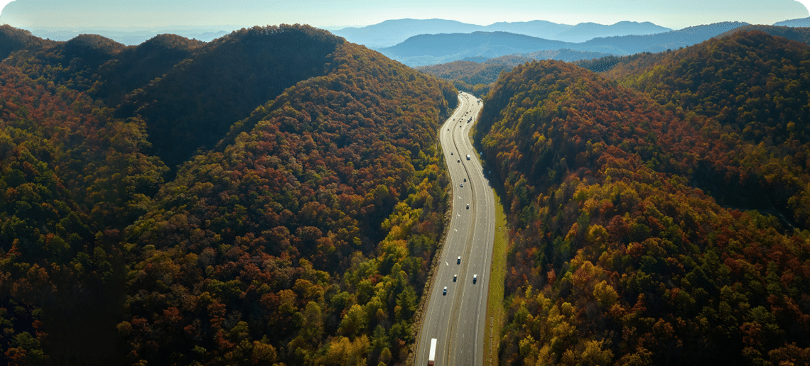 Aerial view of vehicles on a highway with trees on either side and mountains in the distance