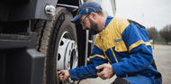 Man in yellow and blue Michelin mechanic jumpsuit putting air in the tire of a semi truck