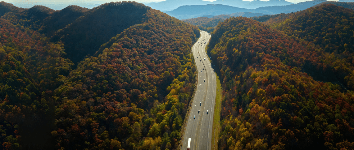 Vue aérienne de véhicules sur une autoroute avec des arbres de chaque côté et des montagnes au loin