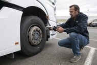 A man with a handheld device next to a bus tire scanning the RFID
