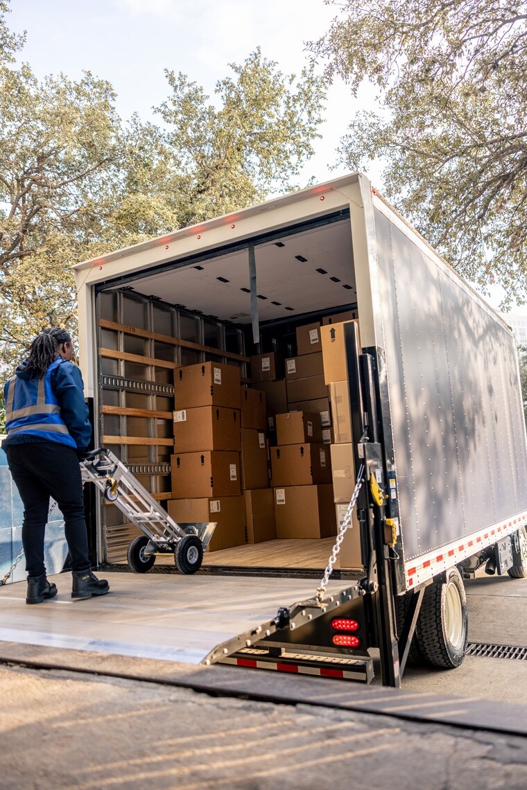 African American female using a dolly to unload stacks of boxes from a box truck