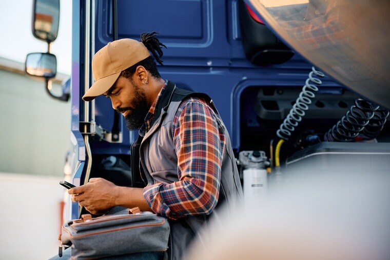 truck driver on cell phone A truck driver sitting on the edge of his semi truck cab looking at a cell phone in his hand