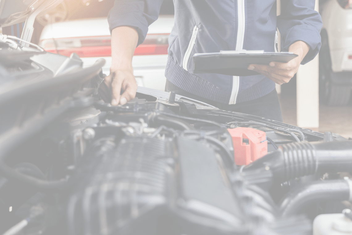 The arms and body of a person holding a clipboard and reviewing a semi truck motor