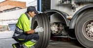 Technician wearing neon green shirt mounting a tire on a semi truck in a service bay