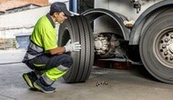 Technician wearing neon green shirt mounting a tire on a semi truck in a service bay