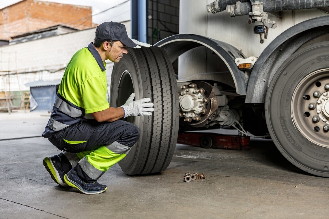 Technicien vêtu d’un gilet de sécurité vert fluo faisant le montage un pneu sur un camion semi-remorque dans un poste de travail