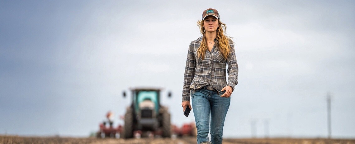 A tractor blurred in the background with a female in a baseball cap walking in the foreground