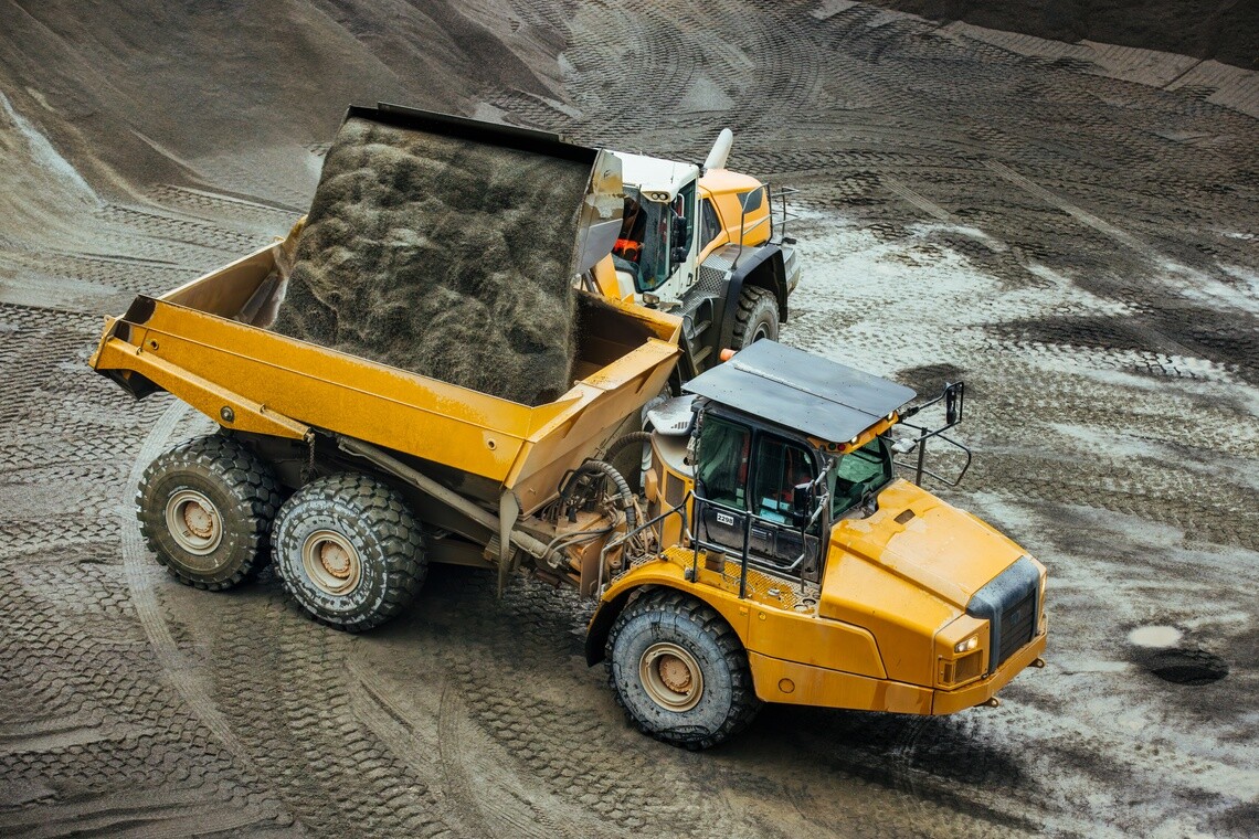 Yellow dump truck being loaded with dirt by a wheel loader in a muddy quarry