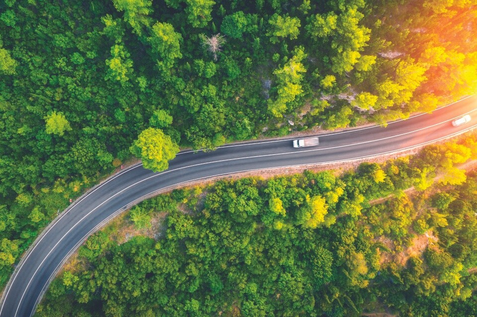 Aerial view of a truck driving along a road surrounded by dense green forest