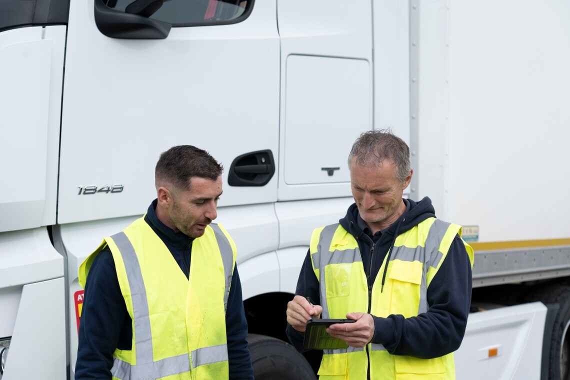 Fleet managers reviewing vehicle performance and maintenance data beside a truck to optimise fleet TCO