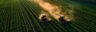 Two agricultural machines working across rows of crops in a field
