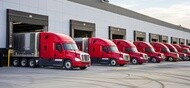 Fleet of semi trucks and trailers lined up at loading bays