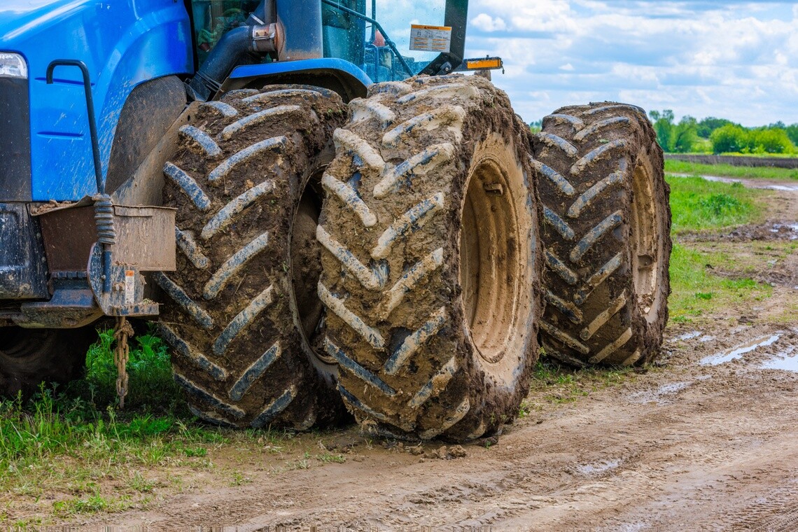 Close-up of an agricultural tractor with mud-covered dual tires in a field.