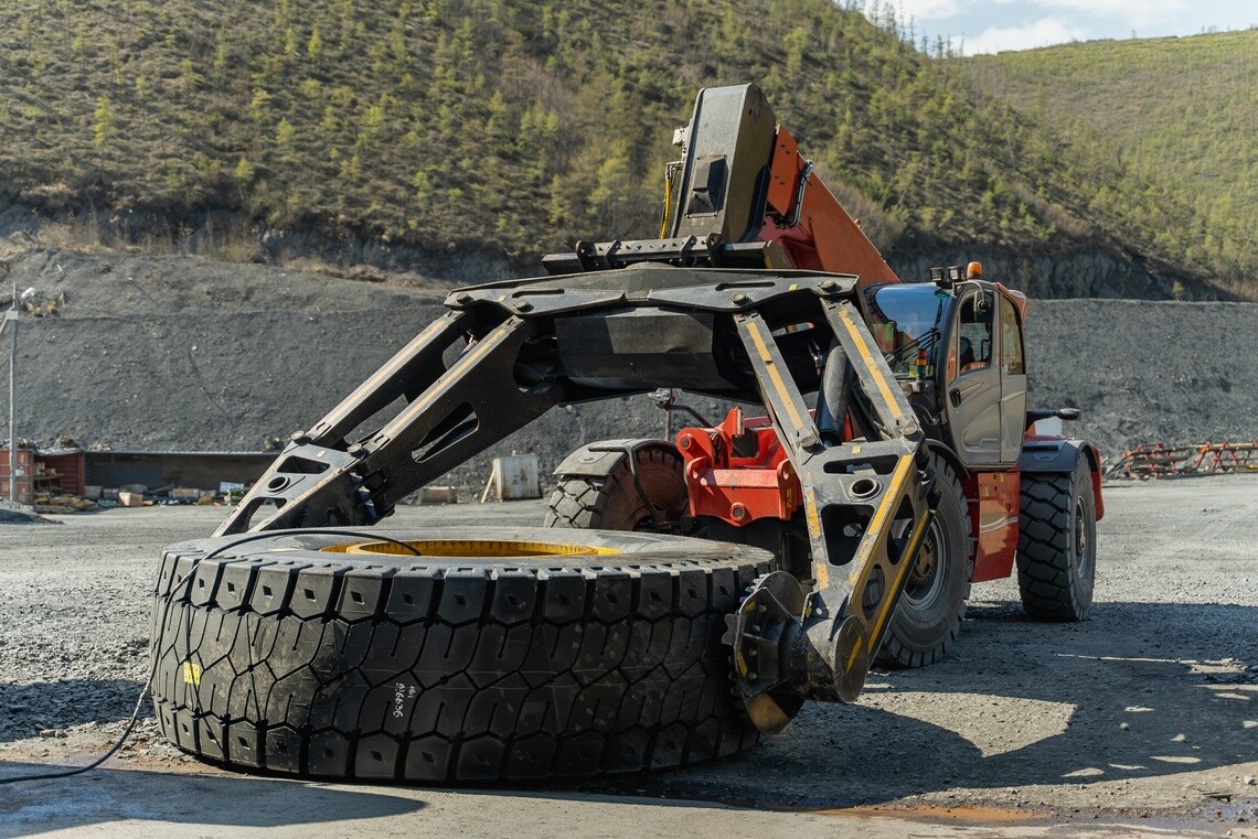 Tire handler lifting and moving a large off-road tire at a quarry.