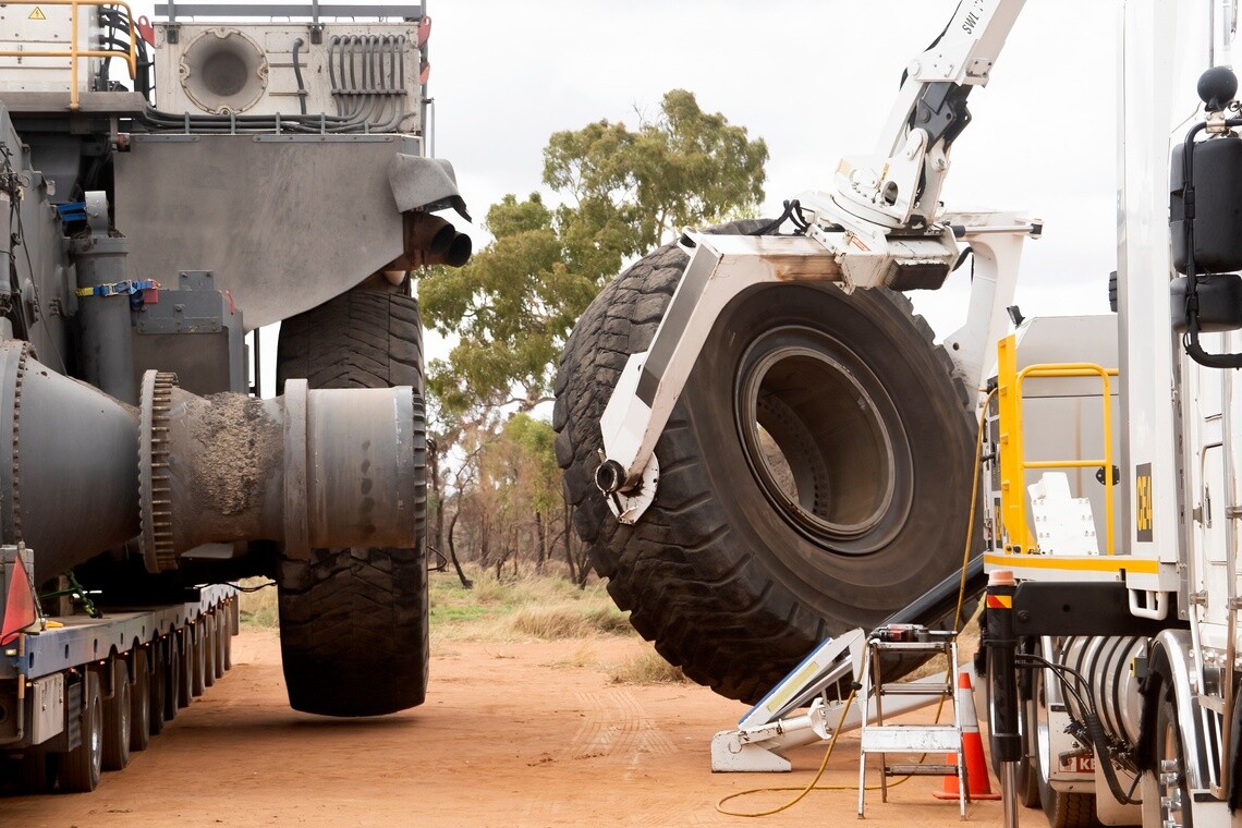 Large off-road tire being removed from heavy equipment using specialized tire-handling equipment.