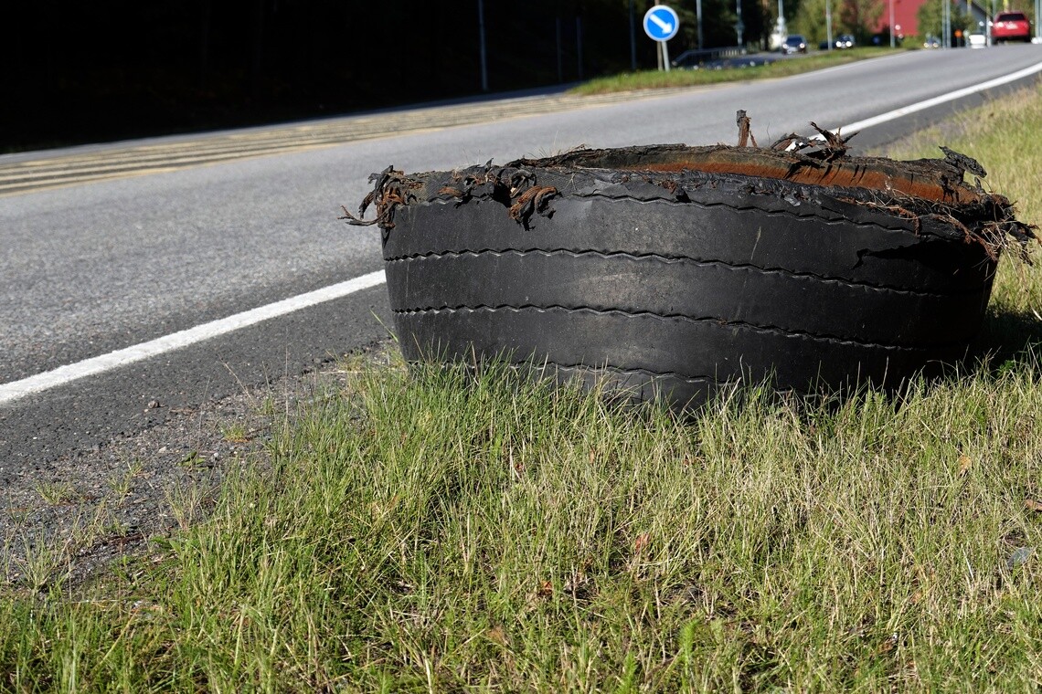 Damaged commercial truck tire lying on the grassy shoulder beside a roadway.