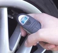 Digital tire pressure gauge being held up to a tire.